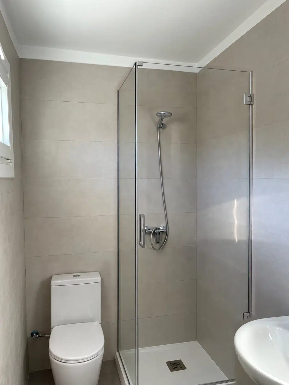 Baño rehabilitado con sanitarios blancos, revestimiento claro y ducha de 70 por 70 centímetros