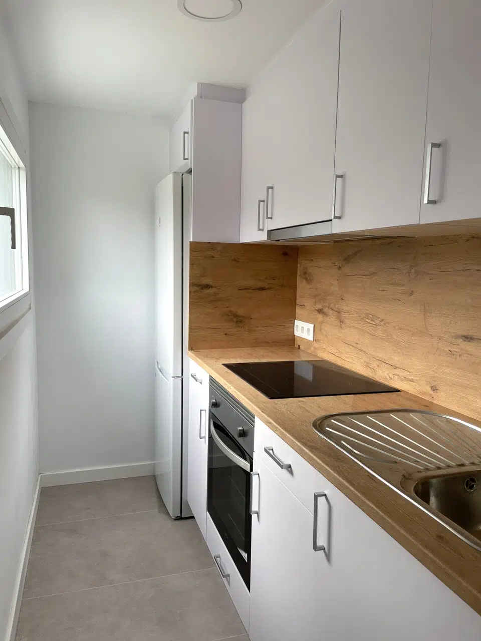 Cocina rehabilitada con muebles blancos, encimera de madera y luz natural