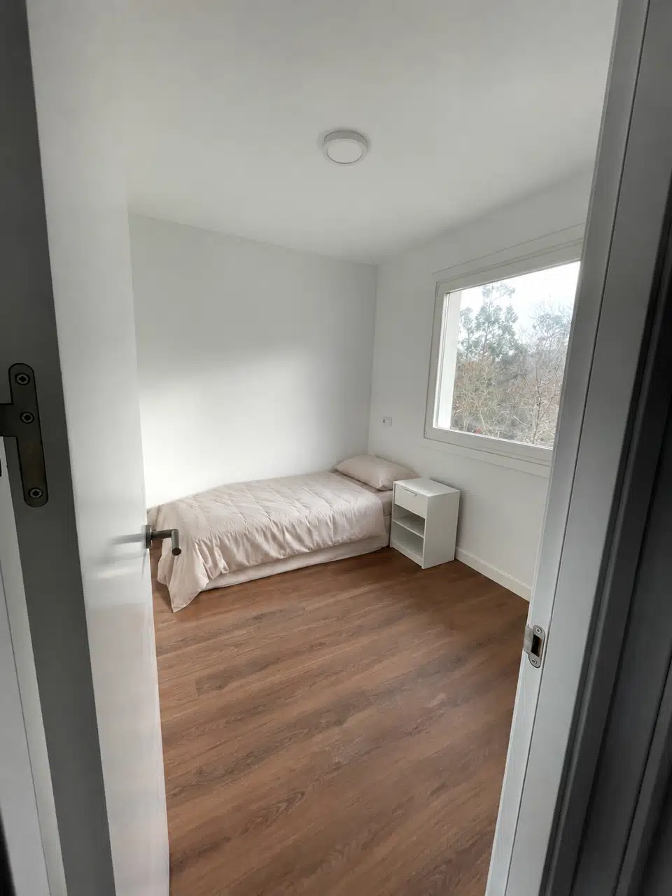 Segundo dormitorio individual con cama junto a la pared y mesilla bajo la ventana