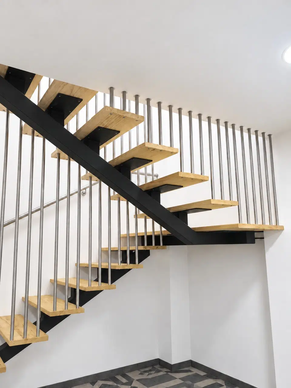 Escalera interior de estructura negra, peldaños de pino y barandilla de varillas metálicas
